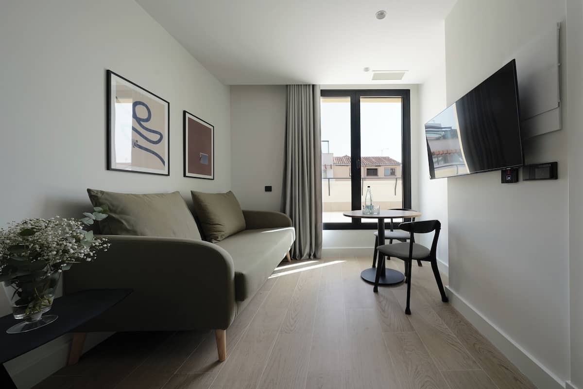 Una sala moderna con un sofá, una mesita con un florero, un televisor montado en la pared y vistas al exterior a través de un ventanal grande.