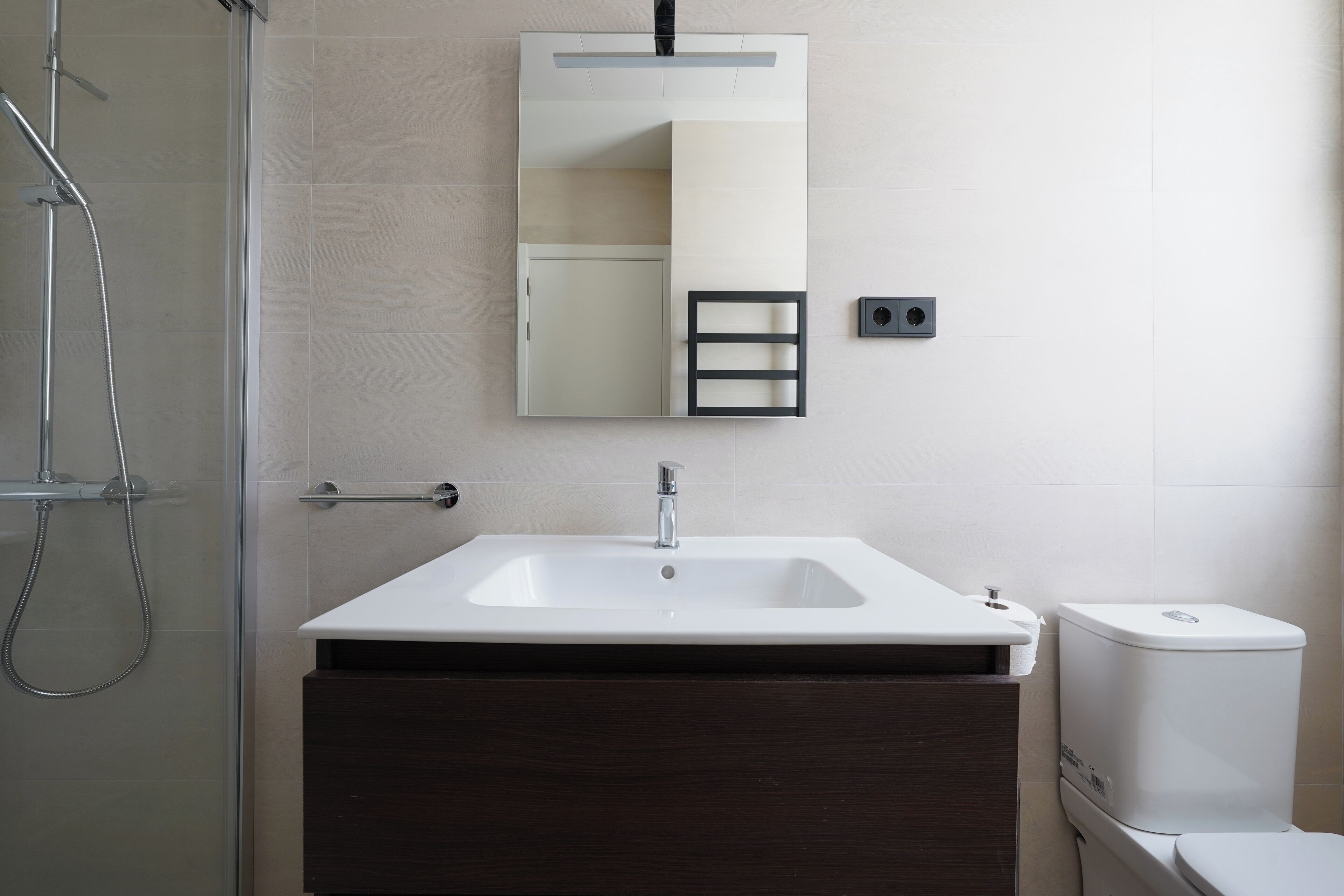 A bathroom with a white sink, dark wooden vanity, a glass shower enclosure, and a toilet.