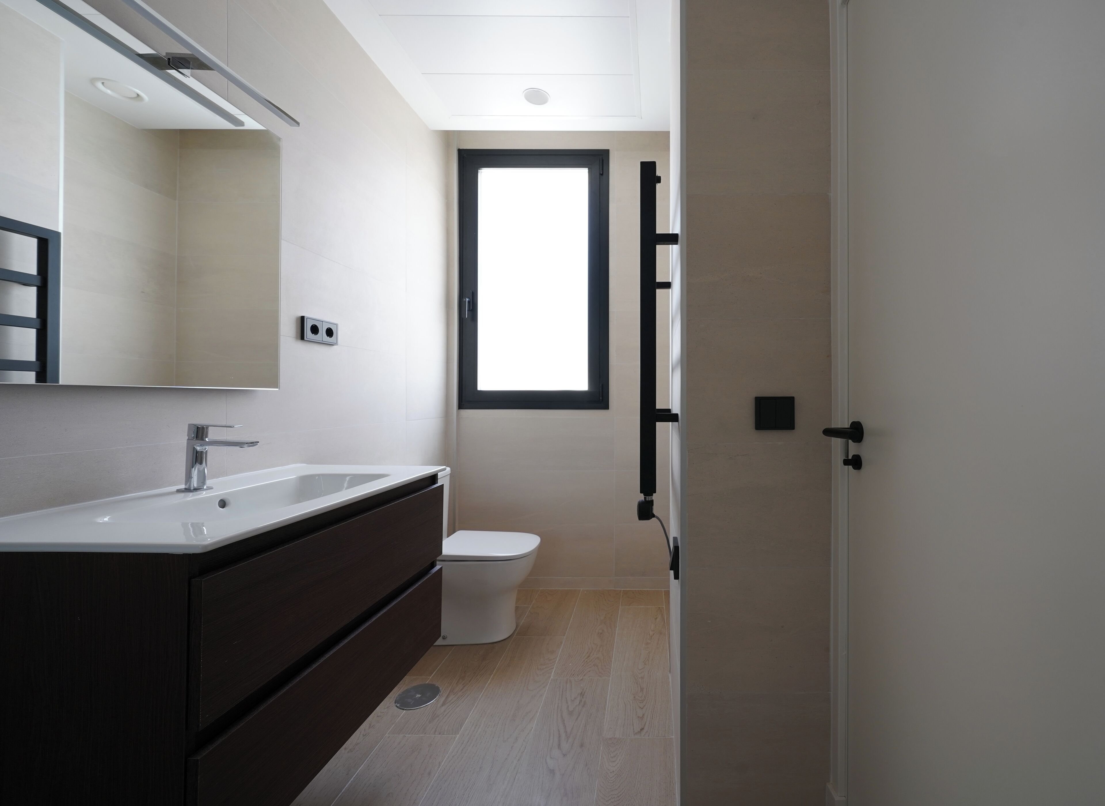 Un baño moderno con lavamanos blanco, tocador oscuro y un inodoro.