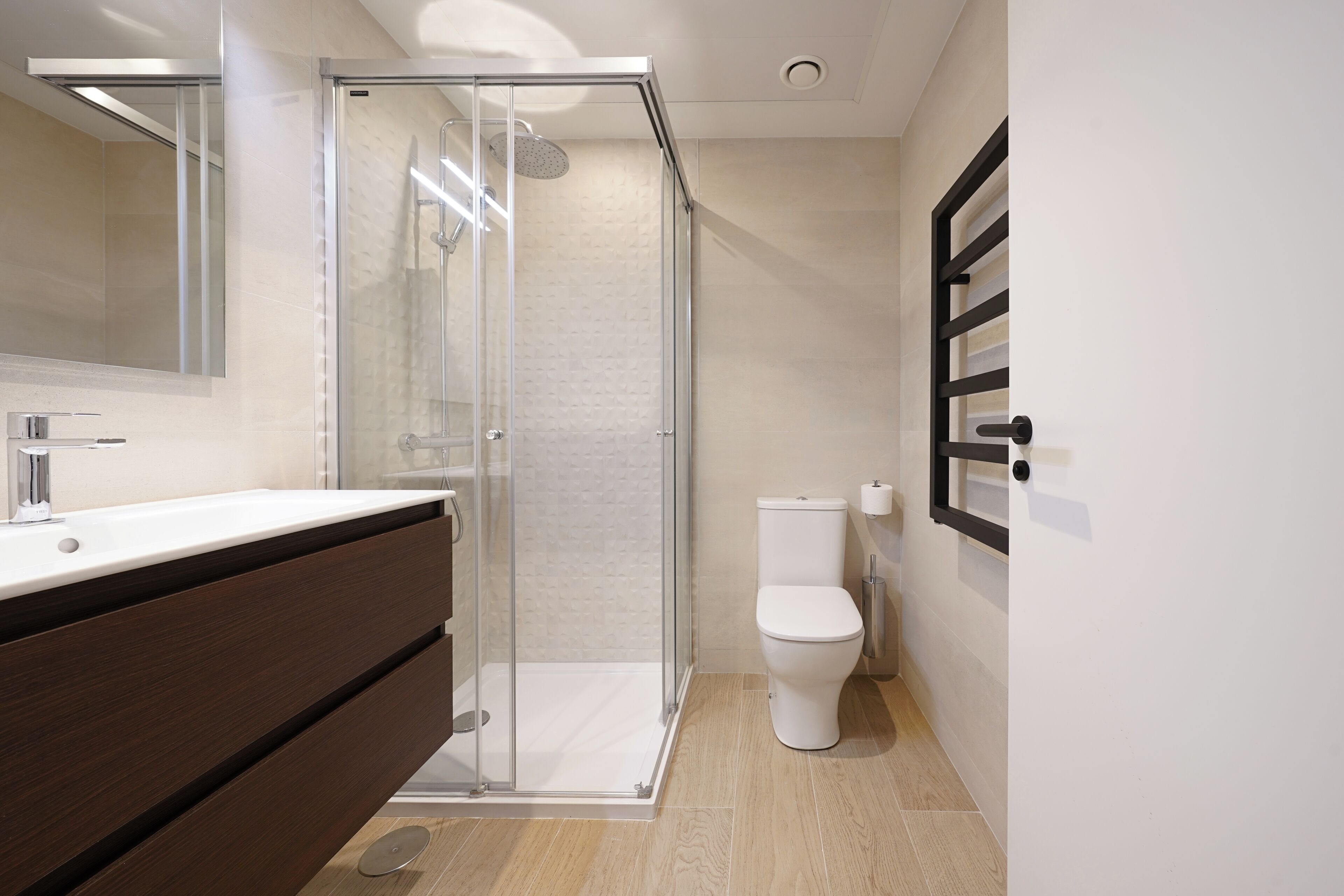 Un baño moderno con cabina de ducha de vidrio, inodoro blanco y tocador de madera.
