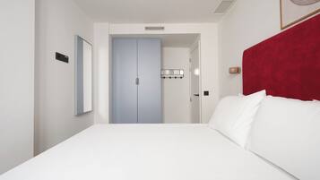 Habitación de hotel con una cama grande, cabecera roja, puerta azul claro y una lámpara fijada a la pared.