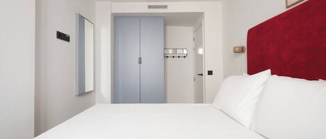 Habitación de hotel con una cama grande, cabecera roja, puerta azul claro y una lámpara fijada a la pared.