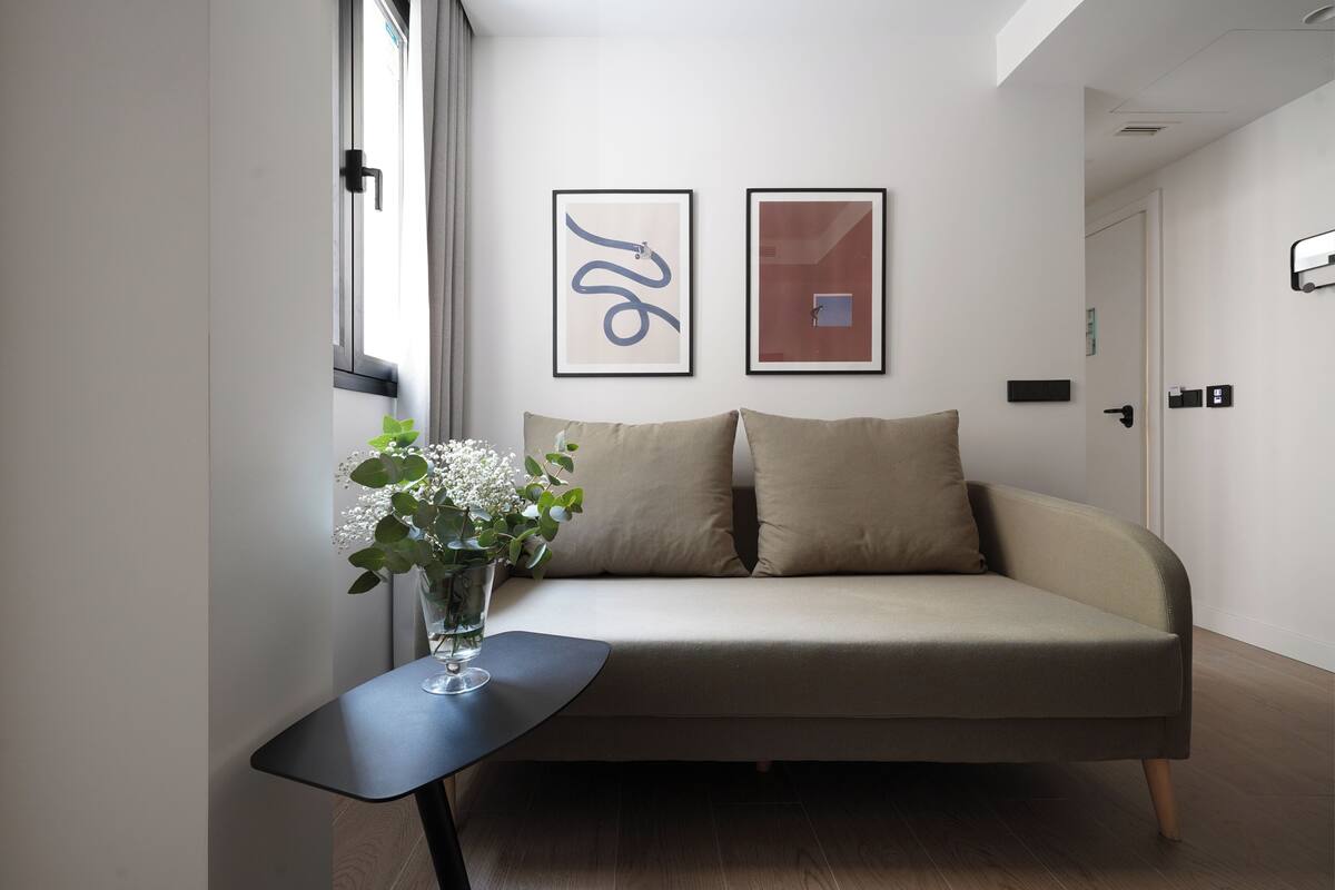 Un moderno salón con un sofá, una mesita baja con un jarrón de flores y dos cuadros enmarcados en la pared.