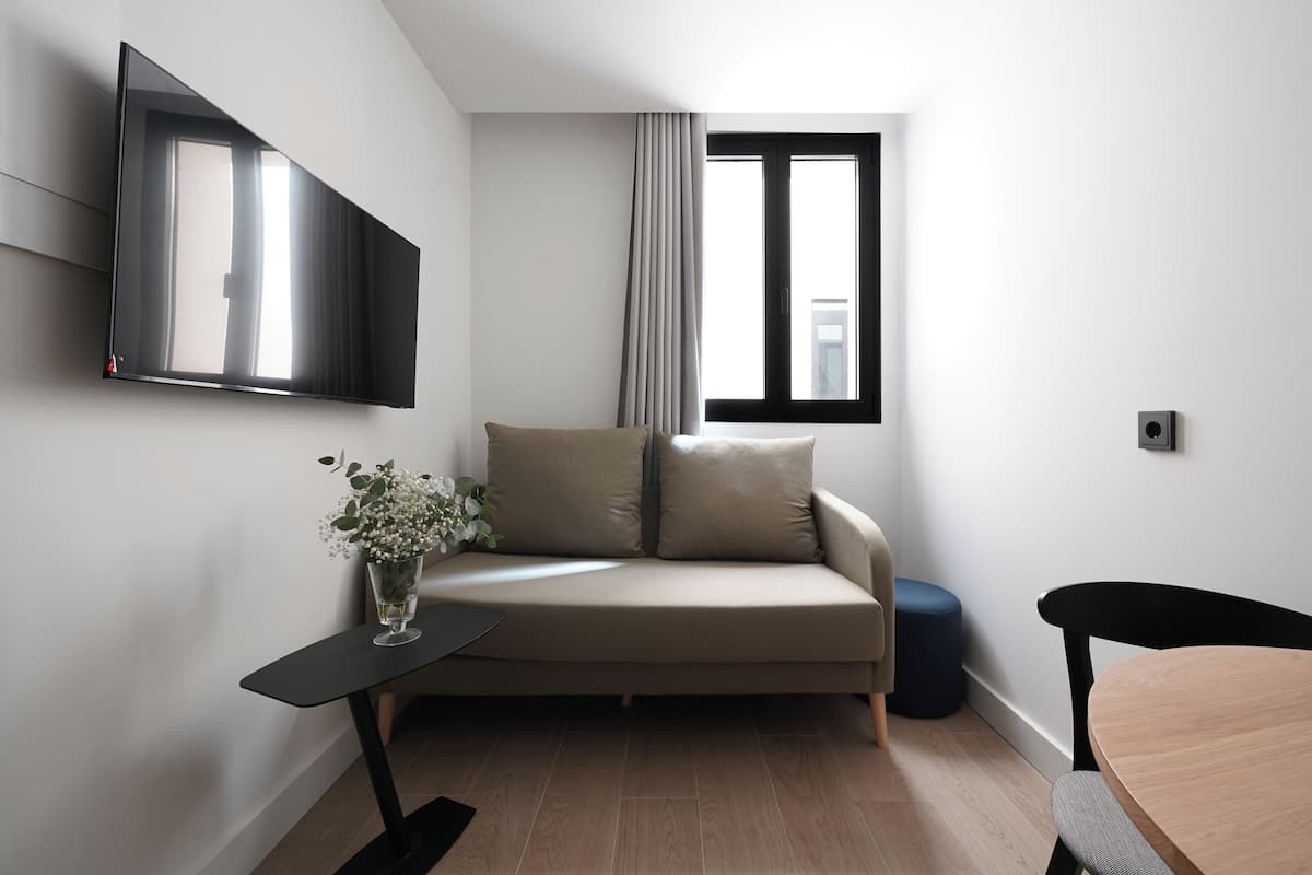 Una sala de estar moderna con un sofá, una mesita con un florero, un televisor montado en la pared y un ventanal con cortinas.
