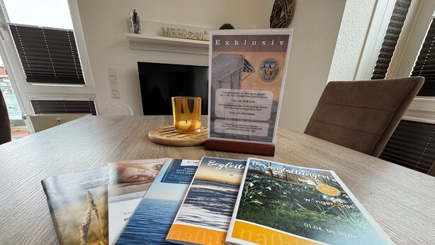 A table with brochures, a candle, and a framed sign. - Meerzeit - im Kaiserhof Wangerooge (Wangerooge)