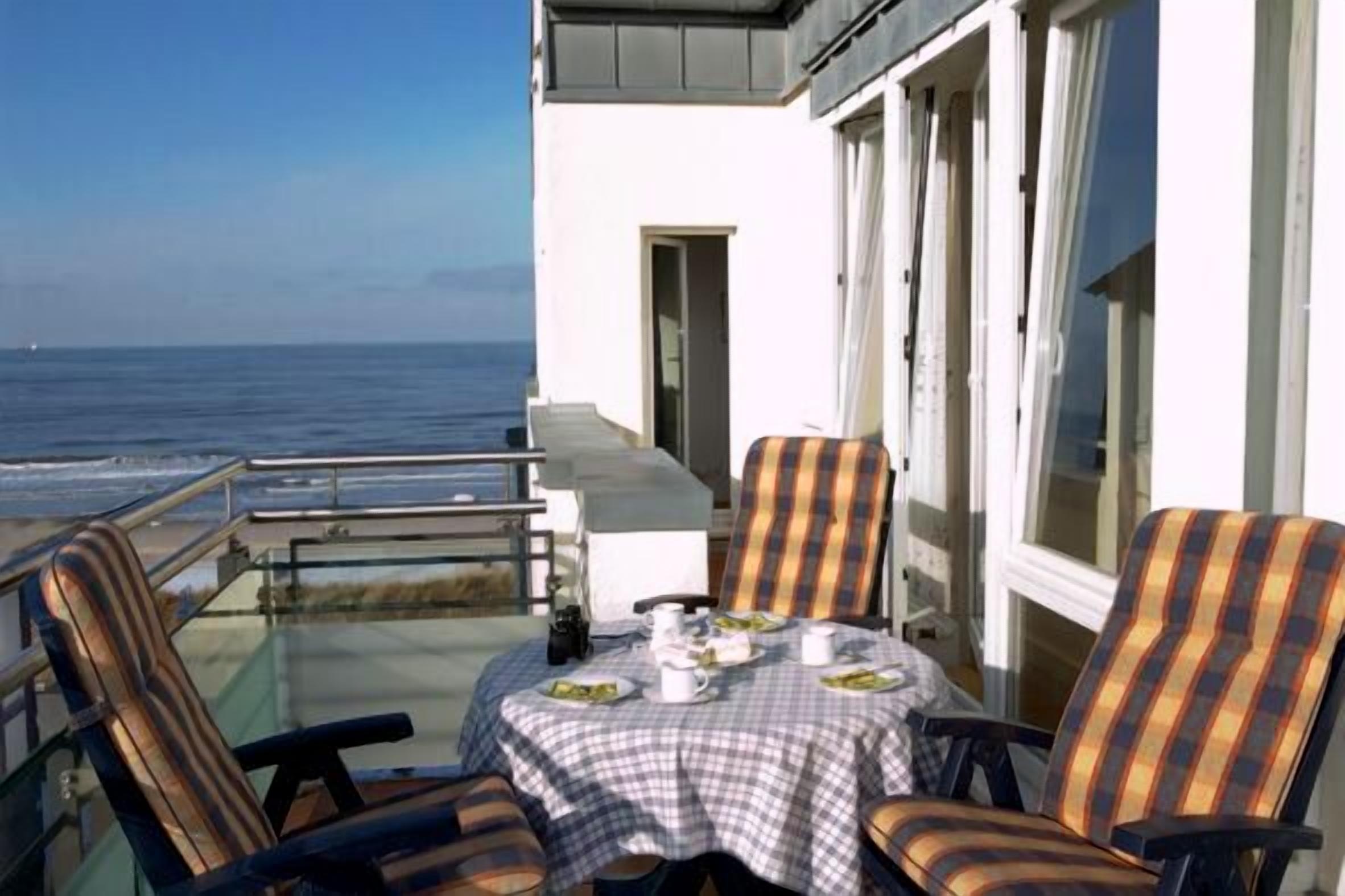 Een balkon met een tafel gedekt voor twee, met uitzicht op zee.