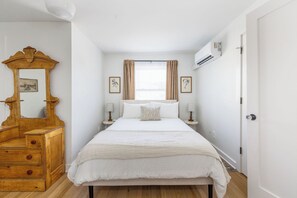 A bedroom with a large bed, a wooden dresser, a mirror, two bedside tables with lamps, and a window with curtains.