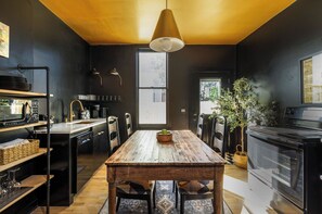 A modern kitchen with a wooden table, black appliances, and a large window.