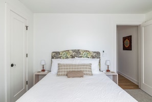 Een slaapkamer met een bed, twee nachtkastjes, een hoofdbord met bloemendesign en een deur.