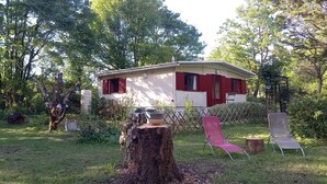 Una piccola casa con tetto rosso e pareti bianche, immersa tra alberi e vegetazione.
