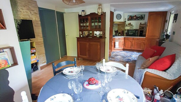Zona pranzo con tavolo rotondo apparecchiato per quattro persone, circondato da sedie. Si intravede una cucina sullo sfondo.