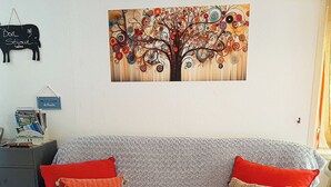Un divano grigio con cuscini rossi e beige, un quadro appeso al muro raffigurante un albero e una lavagna con scritte.