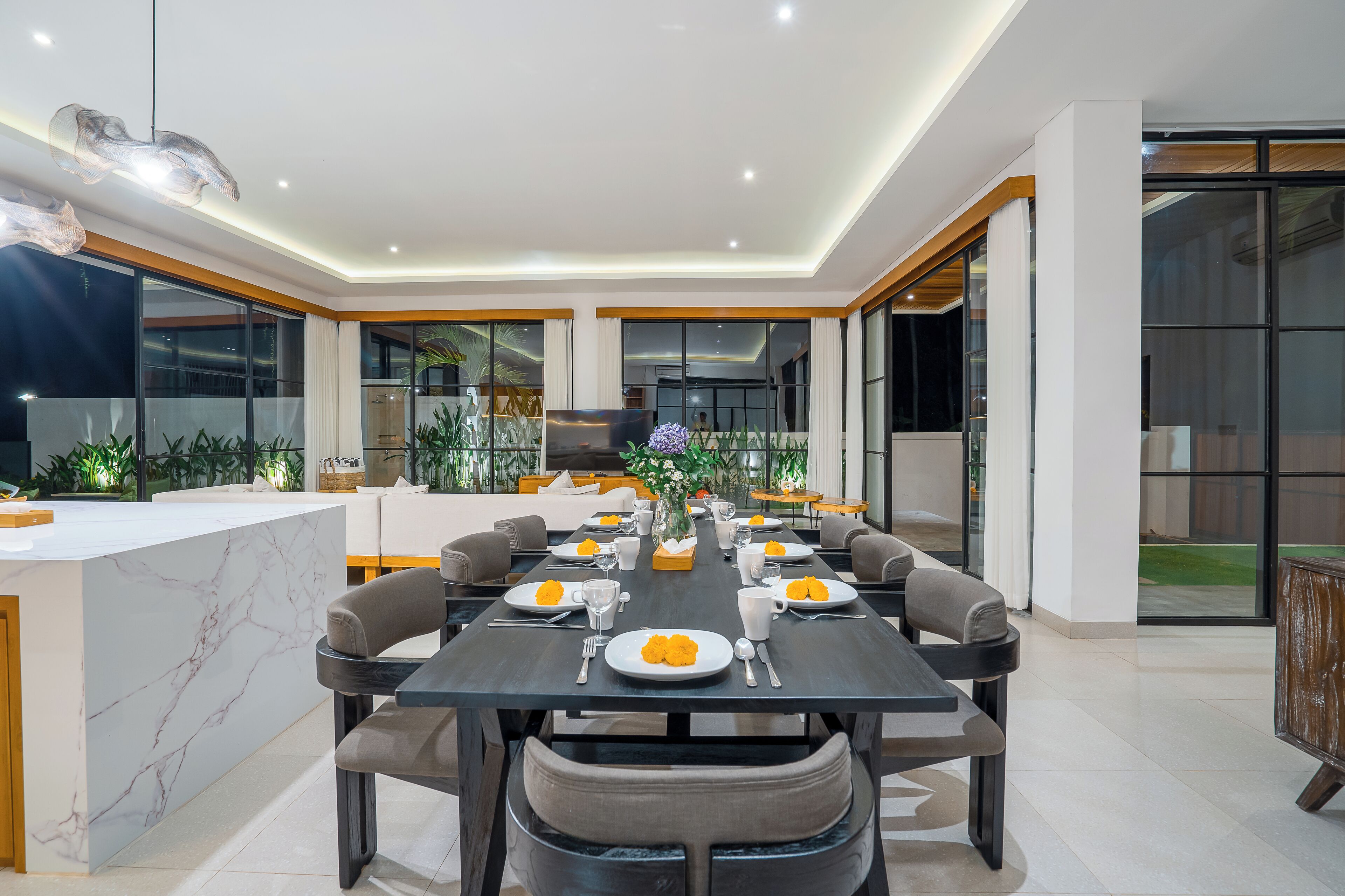 Un comedor moderno con una isla de mármol, diferentes distribuciones de asientos y ventanas amplias que ofrecen vistas al exterior.