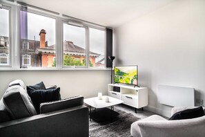 A modern living room with a sofa, a coffee table, a TV, and a window with a view of buildings. - Chic 1BR Wrexham Apt, Walk to Station (Wrexham)