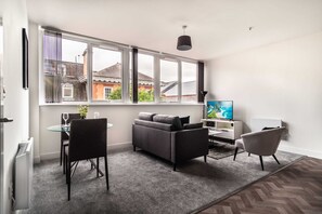 A modern living room with a sofa, a TV, a dining table with chairs, and large windows. - Chic 1BR Wrexham Apt, Walk to Station (Wrexham)