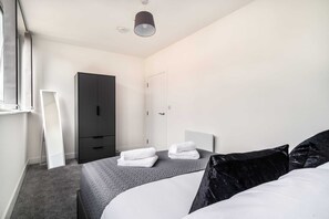 A modern hotel room with a bed, a wardrobe, a mirror, and a door.
