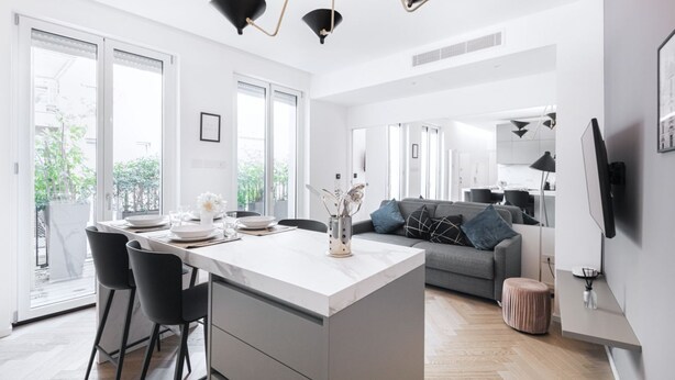 A modern kitchen with a central island, black chairs, and a grey sofa in the living area.