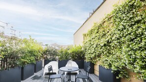 A patio with a round table and four chairs, surrounded by black planters and a wall covered in white flowers.