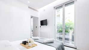 A modern hotel room with a large bed, a flat-screen TV mounted on the wall, and a sliding glass door leading to a balcony.