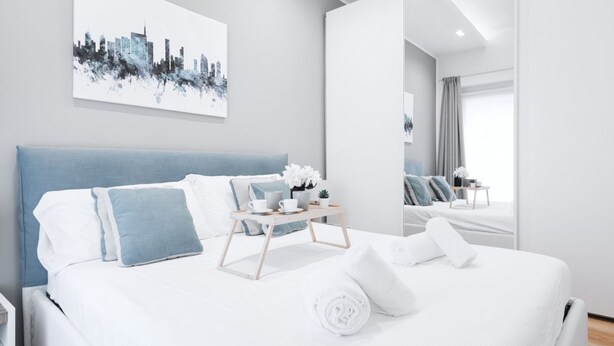 Et moderne hotelværelse med en stor seng, et natbord med bakke og et bybillede på væggen.
