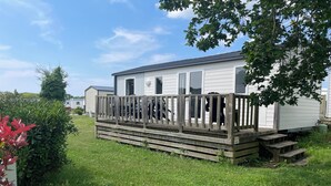 A mobile home with a wooden deck and a small set of stairs leading to the entrance. - XL Mobile-home for 6 -Pommeraie de l'Océan- 4Star (Trégunc)