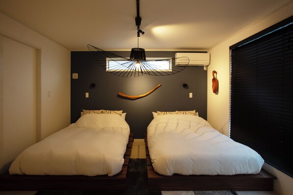 Ein Schlafzimmer mit zwei Betten, einer außergewöhnlichen Deckenleuchte und einem Fenster mit Jalousien.