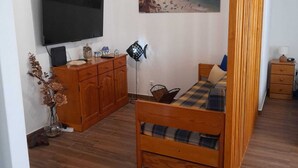 A cozy room with a bed, wooden cabinets, a TV, and a painting of a beach.