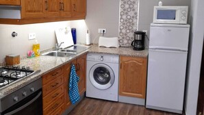 A compact kitchen with wooden cabinets, a washing machine, a microwave, and a stove.