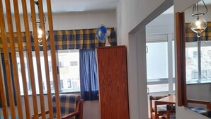 A room with a wooden floor, a plaid sofa, a wooden cabinet, and a dining area with a table and chairs.