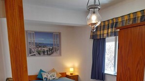 A bedroom with a bed, a nightstand, a lamp, a window with curtains, and a wooden floor.