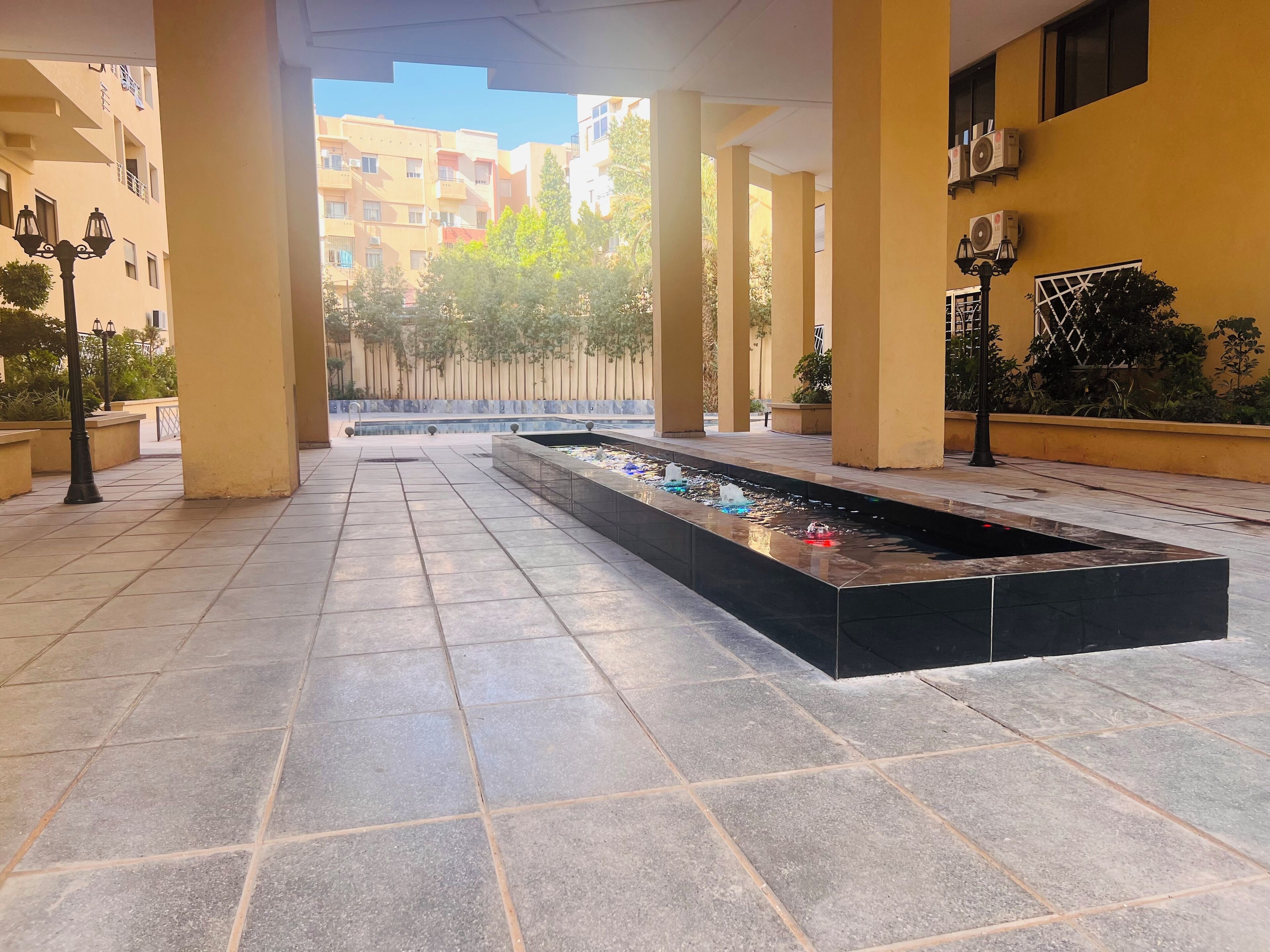 A covered outdoor area with a rectangular water feature, tiled flooring, and columns.
