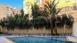 A swimming pool with a tiled deck, surrounded by a low wall and trees. - 2 Bedroom Apartment in Marrakech (Marrakech)