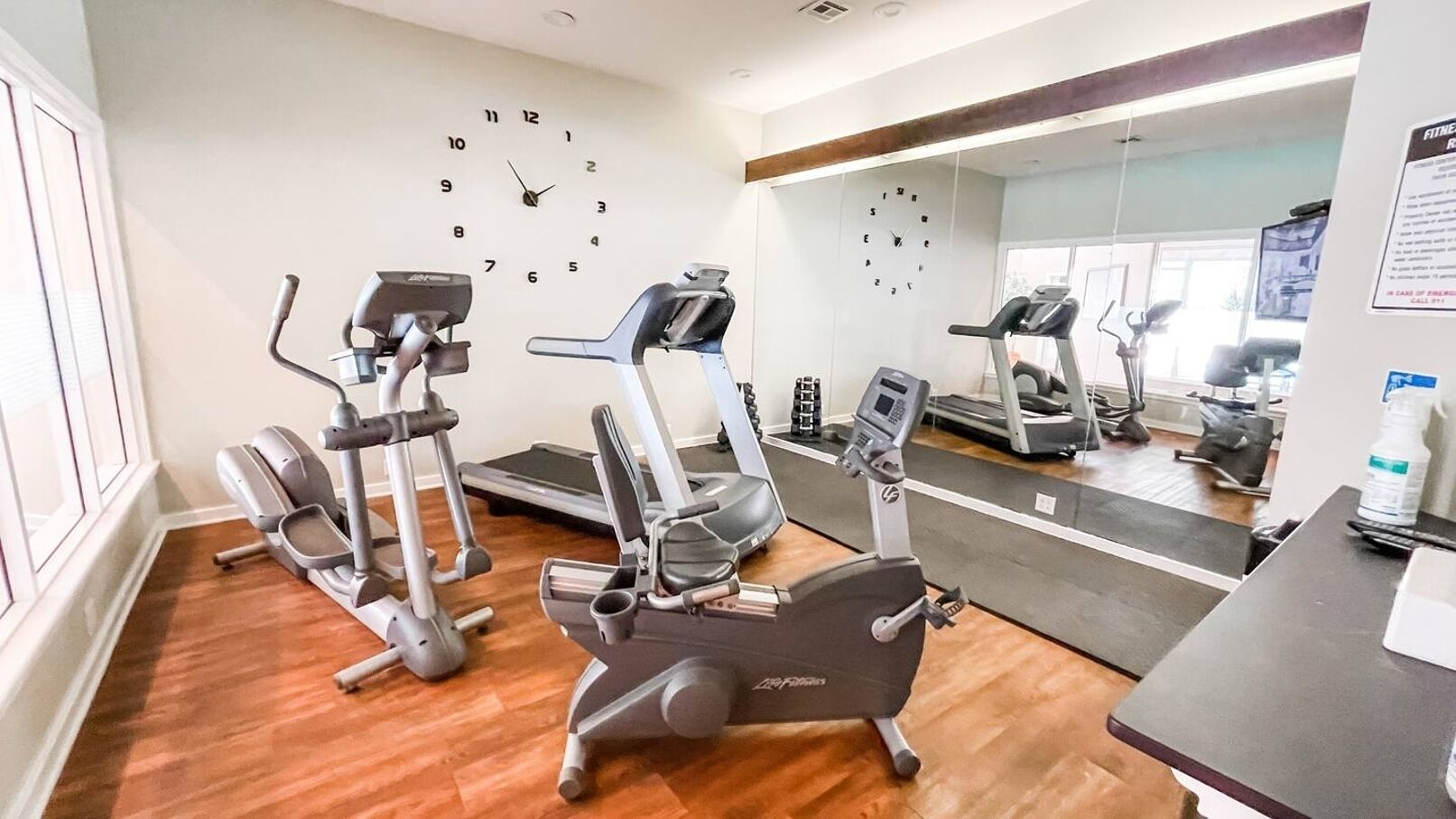 Ein Fitnessraum mit Laufbändern, Spiegel und Wanduhr.