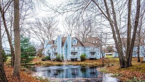 A large blue house with multiple balconies and a pond in the foreground.