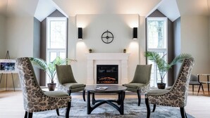 A modern living room with a fireplace, two armchairs, a coffee table, and large windows.