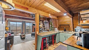 L’intérieur chaleureux d’un chalet avec un plafond en bois, un coin cuisine doté d’un bar vert et un sapin de Noël.