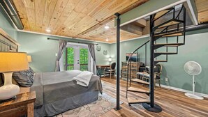 Une chambre avec un plafond en bois, un lit, un bureau et un escalier en colimaçon.