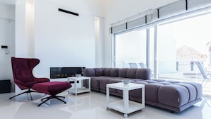 A modern living room with a large window, a grey sofa, a red chair, and a white coffee table. - Marousi 2 Bd Luxury Living w Shared Pool (Marousi)