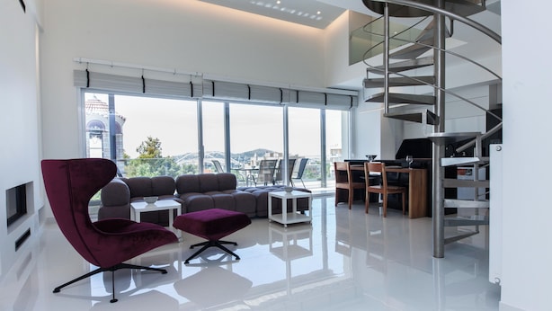 A modern living room with a large window, a curved staircase, and a seating area with a red chair and ottoman. - Marousi 2 Bd Luxury Living w Shared Pool (Marousi)