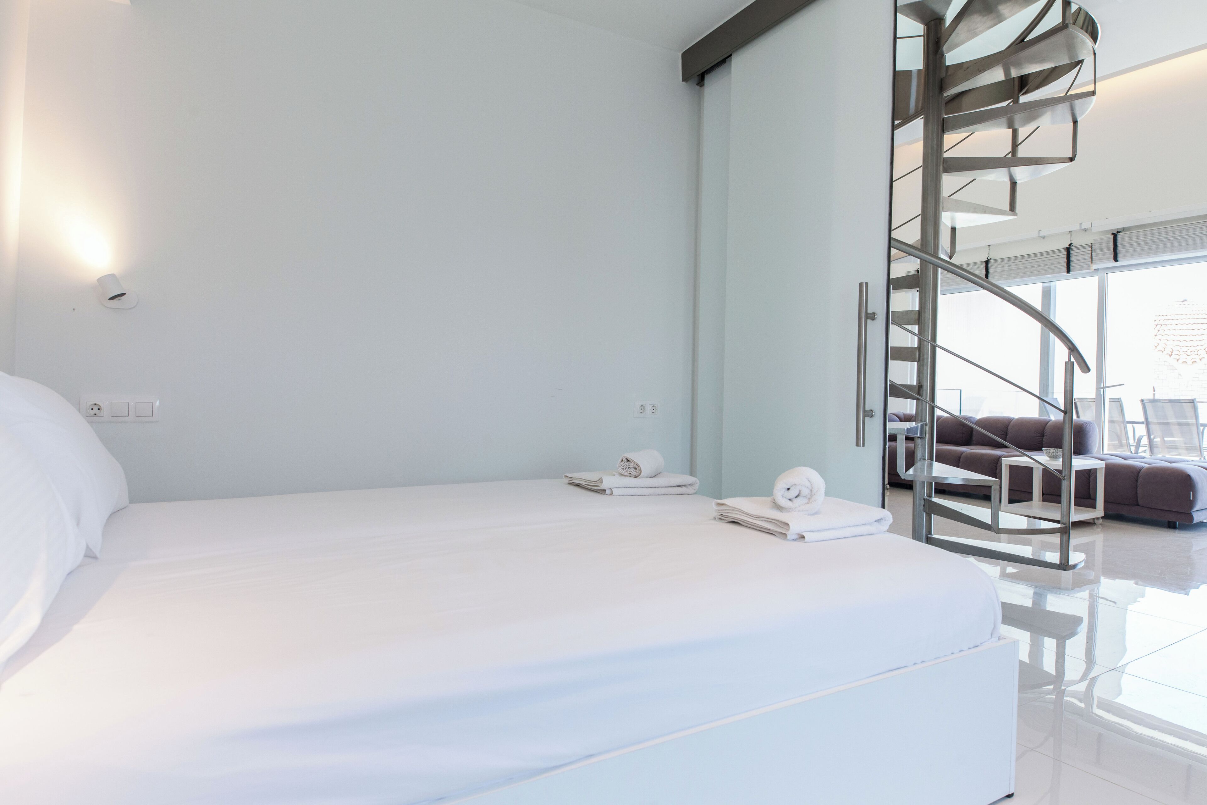 A modern hotel room with a large bed, a spiral staircase, and a view of the city.