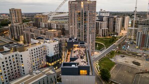 Un quartier urbain moderne, caractérisé par de grands immeubles, une grande roue bien visible et une rue très fréquentée.