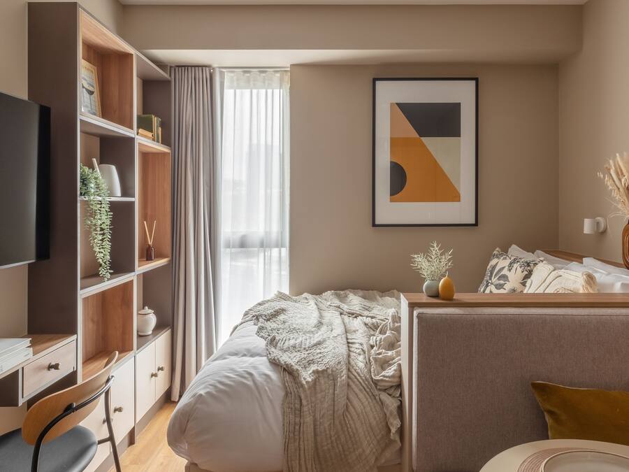 Una moderna camera d'albergo con un letto, una scrivania, una libreria e un'ampia finestra con tende.