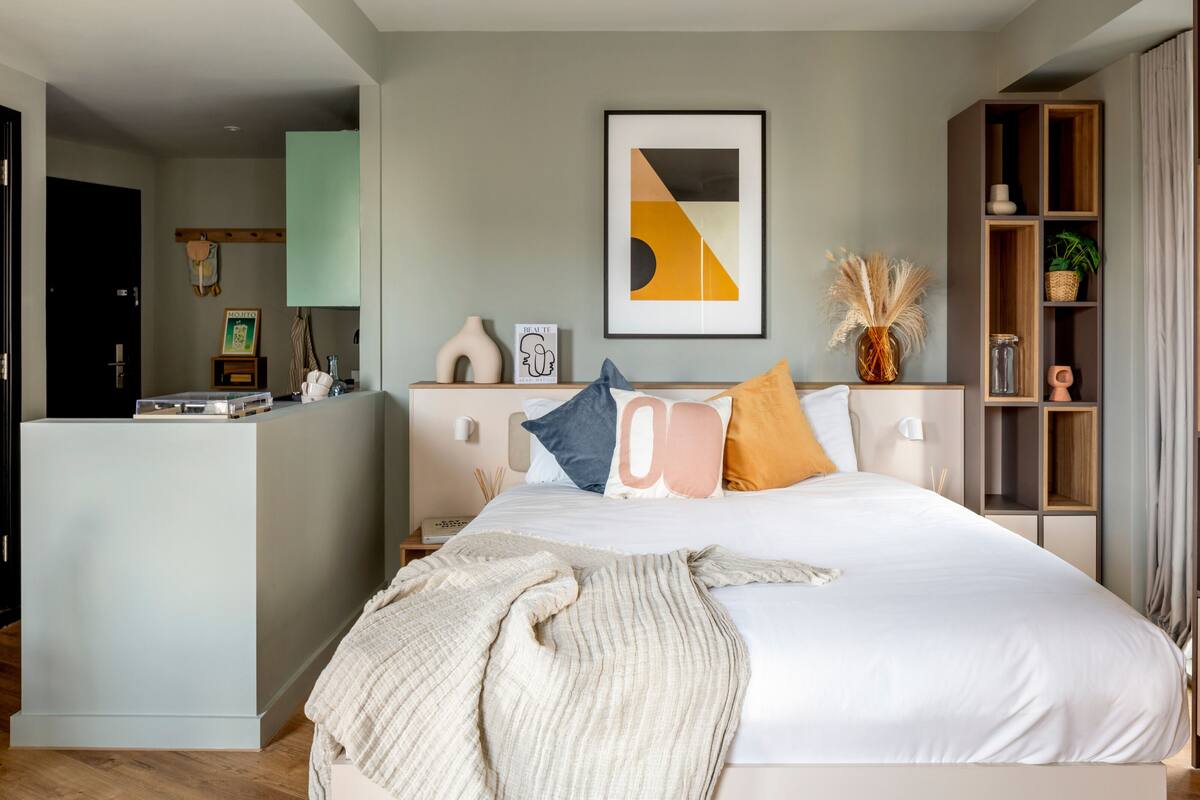 A modern bedroom with a large bed, a bedside table, a small desk, and a bookshelf.