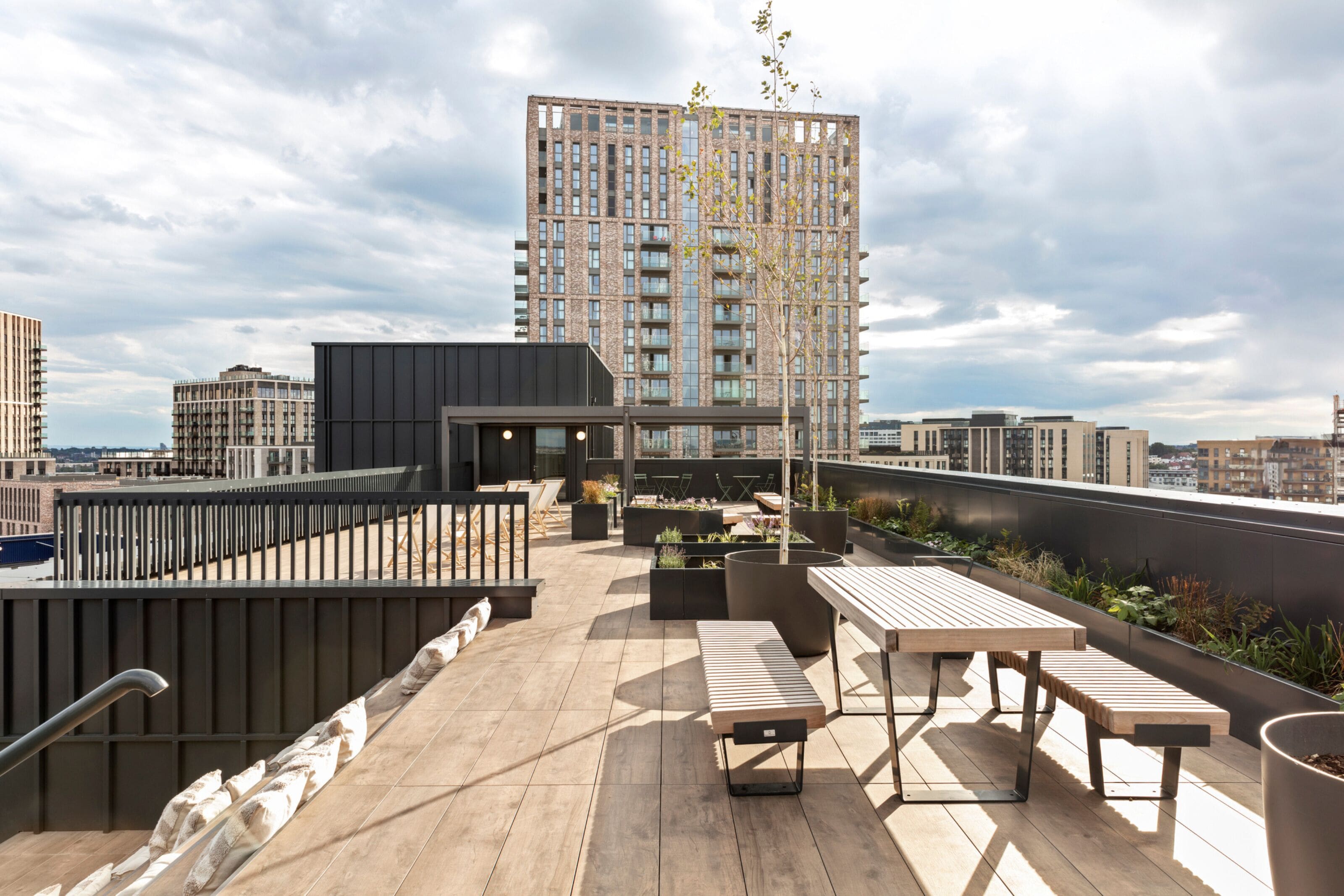 Una terraza en la azotea con cubierta de madera, zonas de estar y vista a un edificio alto al fondo.