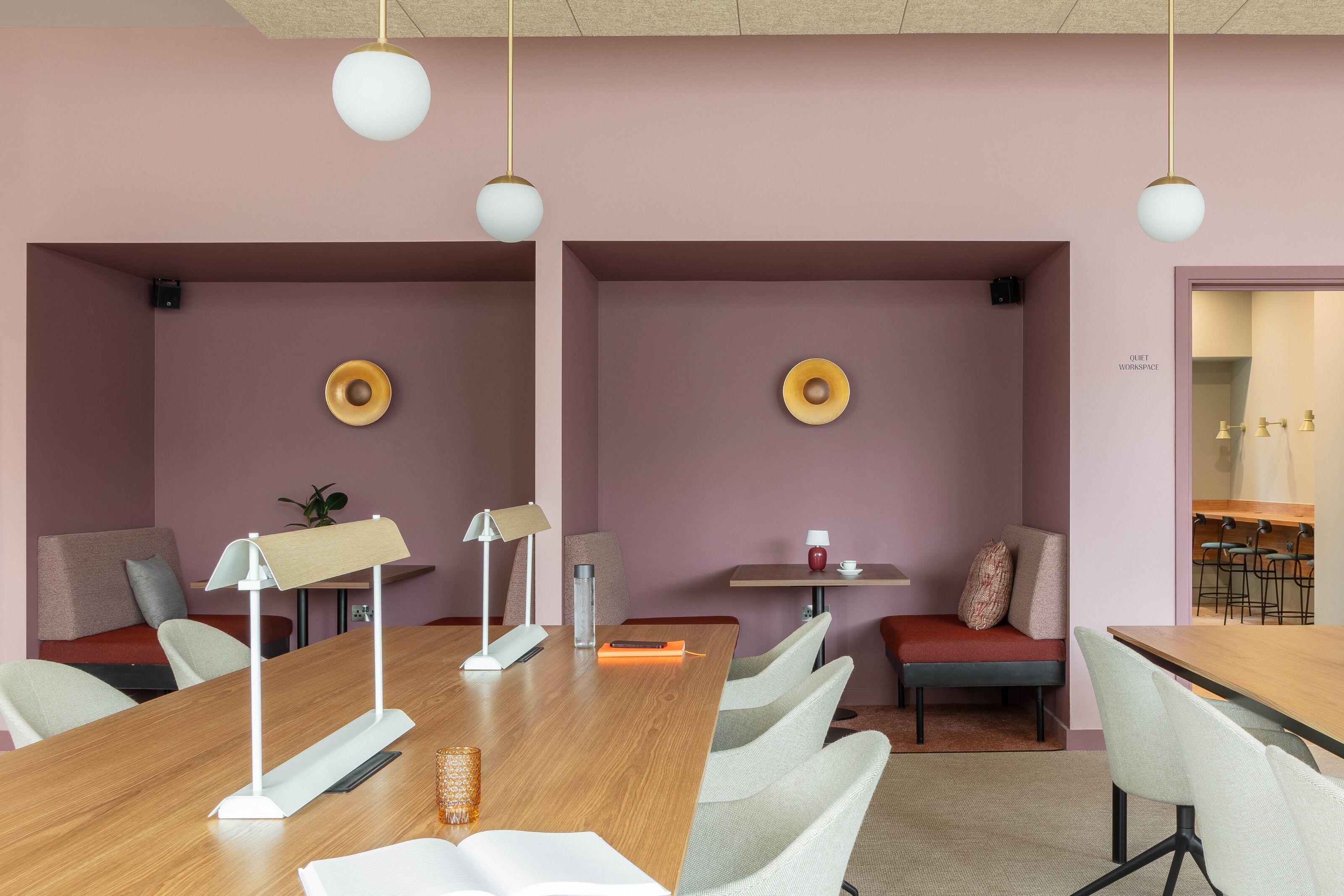 Una sala de reuniones moderna con una mesa de madera alargada, sillas blancas y una pequeña zona de estar con un banco rojo.