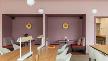 A modern meeting room with a long wooden table, white chairs, and a small seating area with a red bench.