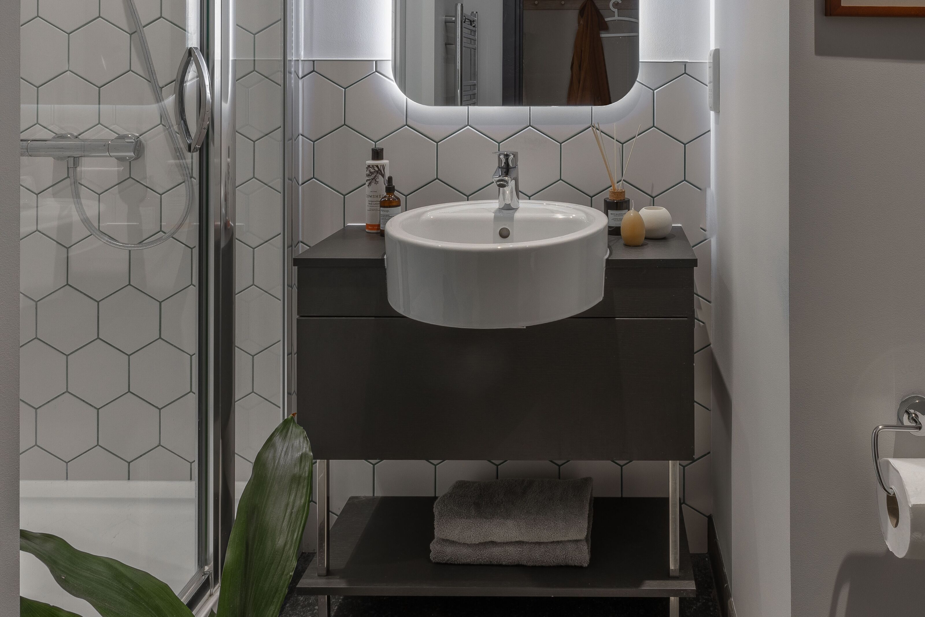 A bathroom with a white sink, dark vanity, and a glass shower enclosure.
