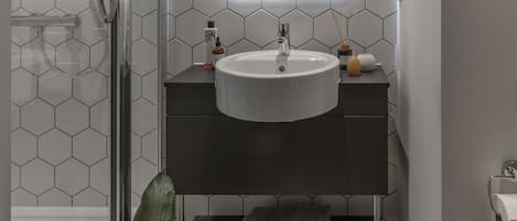 A bathroom with a white sink, dark vanity, and a glass shower enclosure.