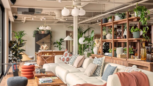 Un salon moderne avec un canapé d’angle, une table basse et une bibliothèque remplie de plantes et d’objets décoratifs.
