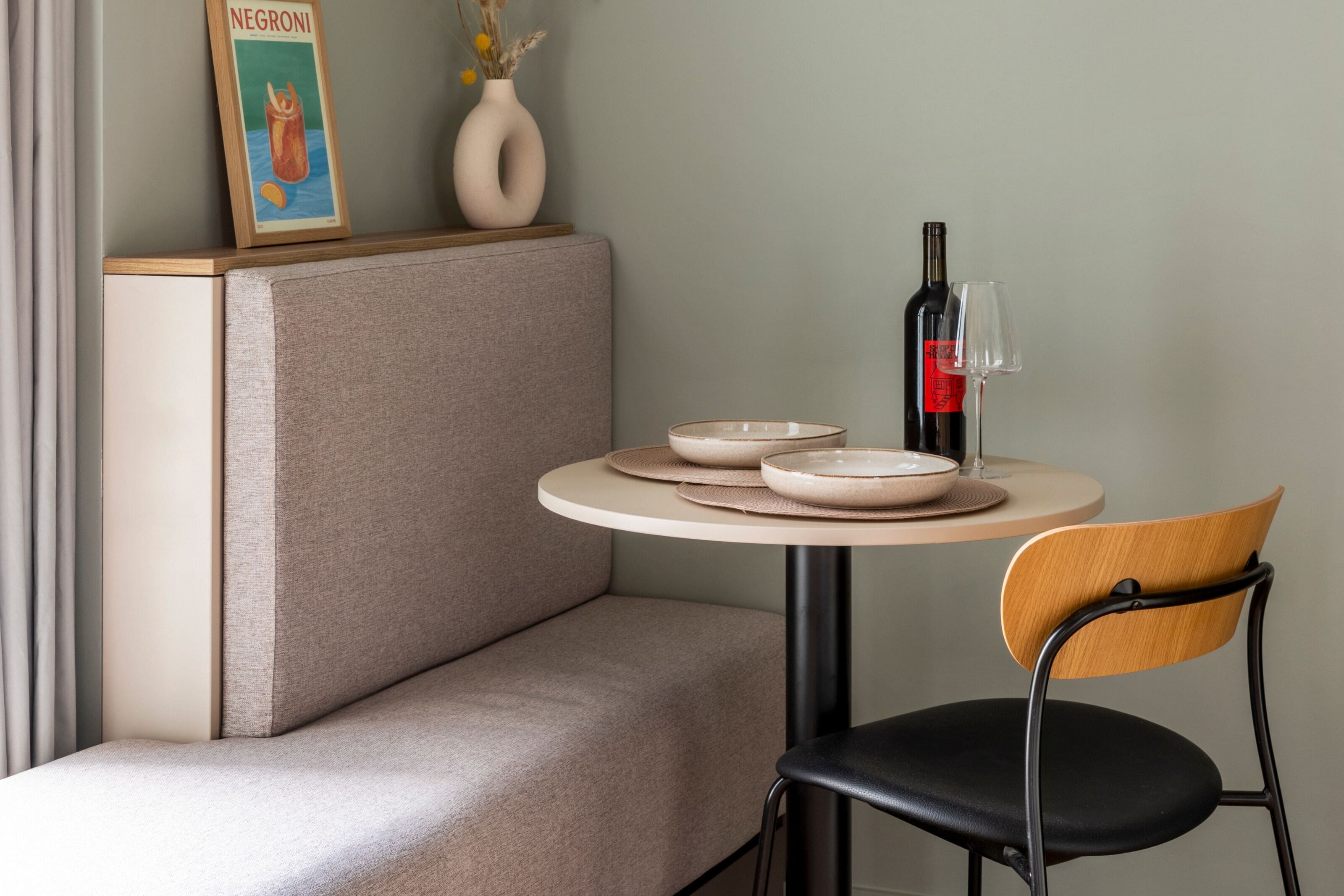 A dining area with a round table, a chair, a sofa, a wine bottle, and a glass.